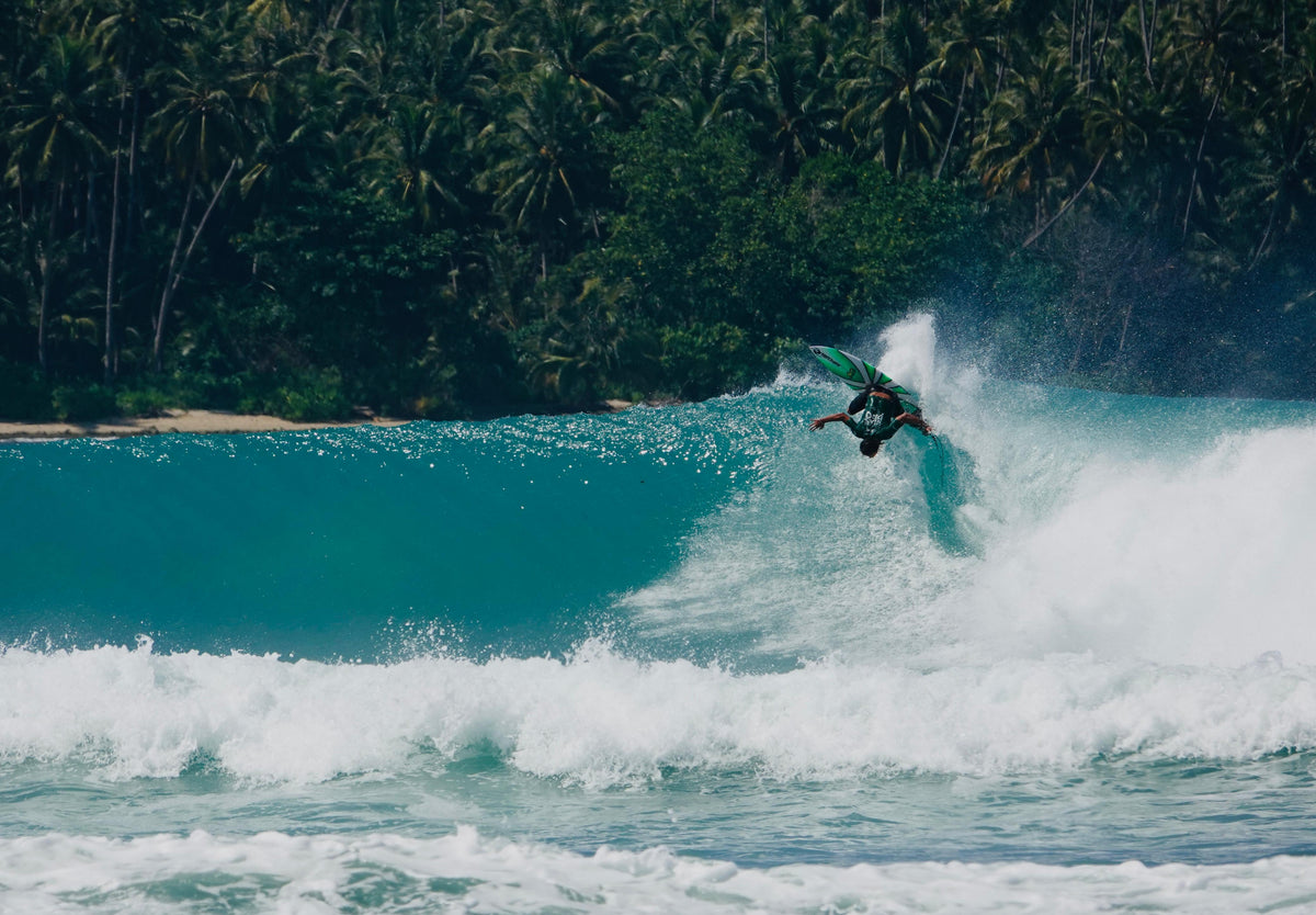A surfer launching an air off a turquoise wave in front of palm trees