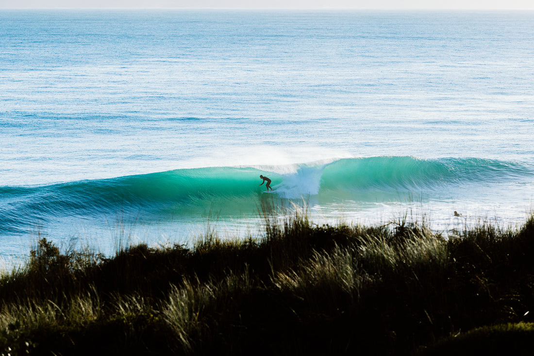 A surfer on an empty, peeling wave below green coastal hills