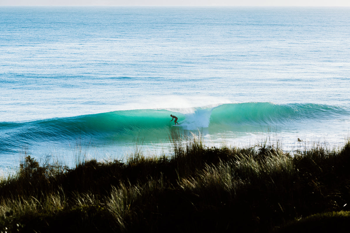 A surfer on an empty, peeling wave below green coastal hills