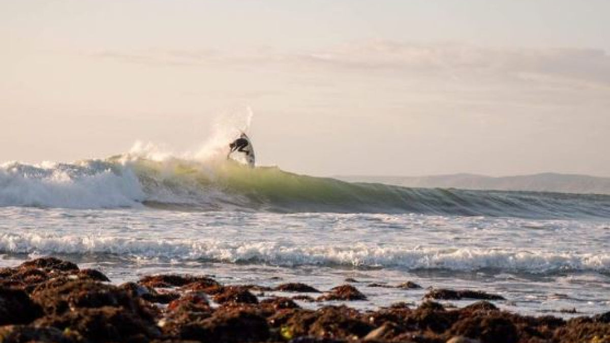 A surfer on a reef break at sunset